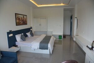 Una habitación de hotel con cama, escritorio, silla, armario y un cuadro en la pared.