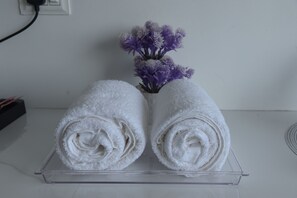 Two rolled white towels on a clear tray with a vase of purple flowers in the background.