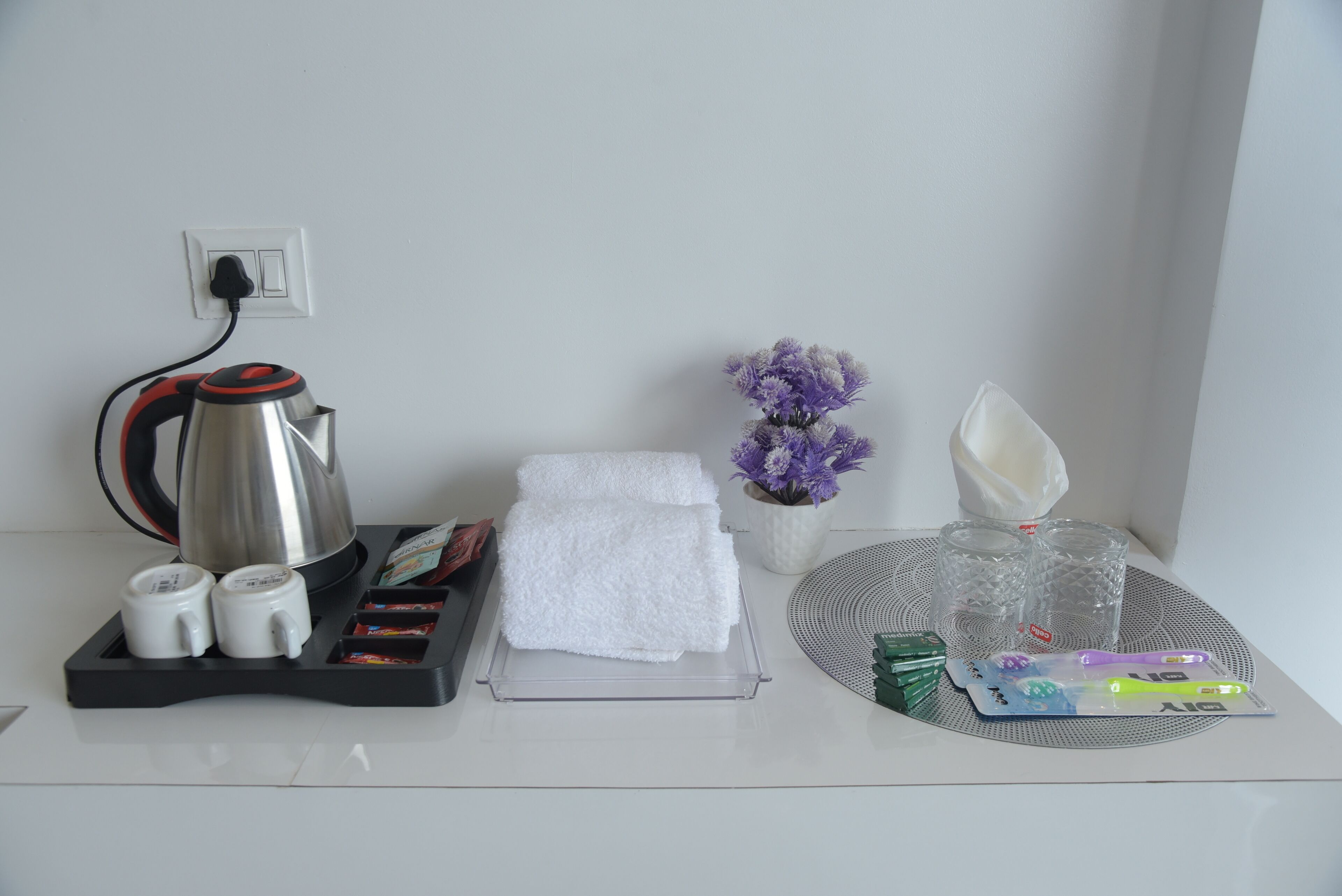 Et hotelværelse med kaffemaskine, te-service, håndklæder, en vase med blomster og toiletartikler på et bakke.