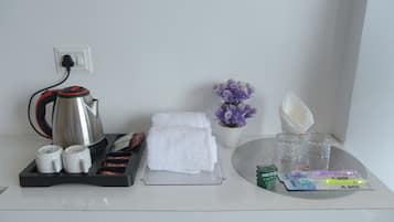 A hotel room with a coffee maker, tea set, towels, a vase with flowers, and toiletries on a tray.