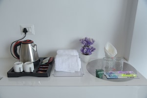 Habitación de hotel con cafetera, tetera, toallas, un jarrón con flores y artículos de aseo en una bandeja.