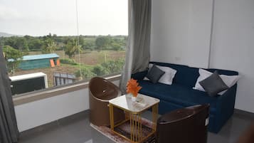 A room with a blue sofa, a small table with a vase, and a view of a green landscape through a window.