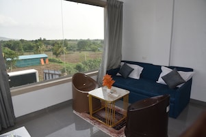 Una habitación con un sofá azul, una mesita con un florero y vistas a un paisaje verde a través de una ventana.