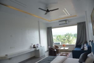 Una habitación de hotel moderna con cama, escritorio, silla, ventilador de techo y vista a palmeras.