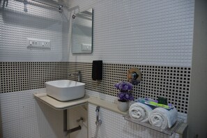 Un baño con un lavamanos blanco, un espejo, un perchero para toallas y una ducha.