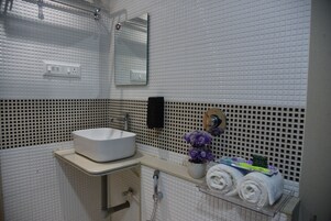 Un baño con un lavamanos blanco, un espejo, un perchero para toallas y una ducha.
