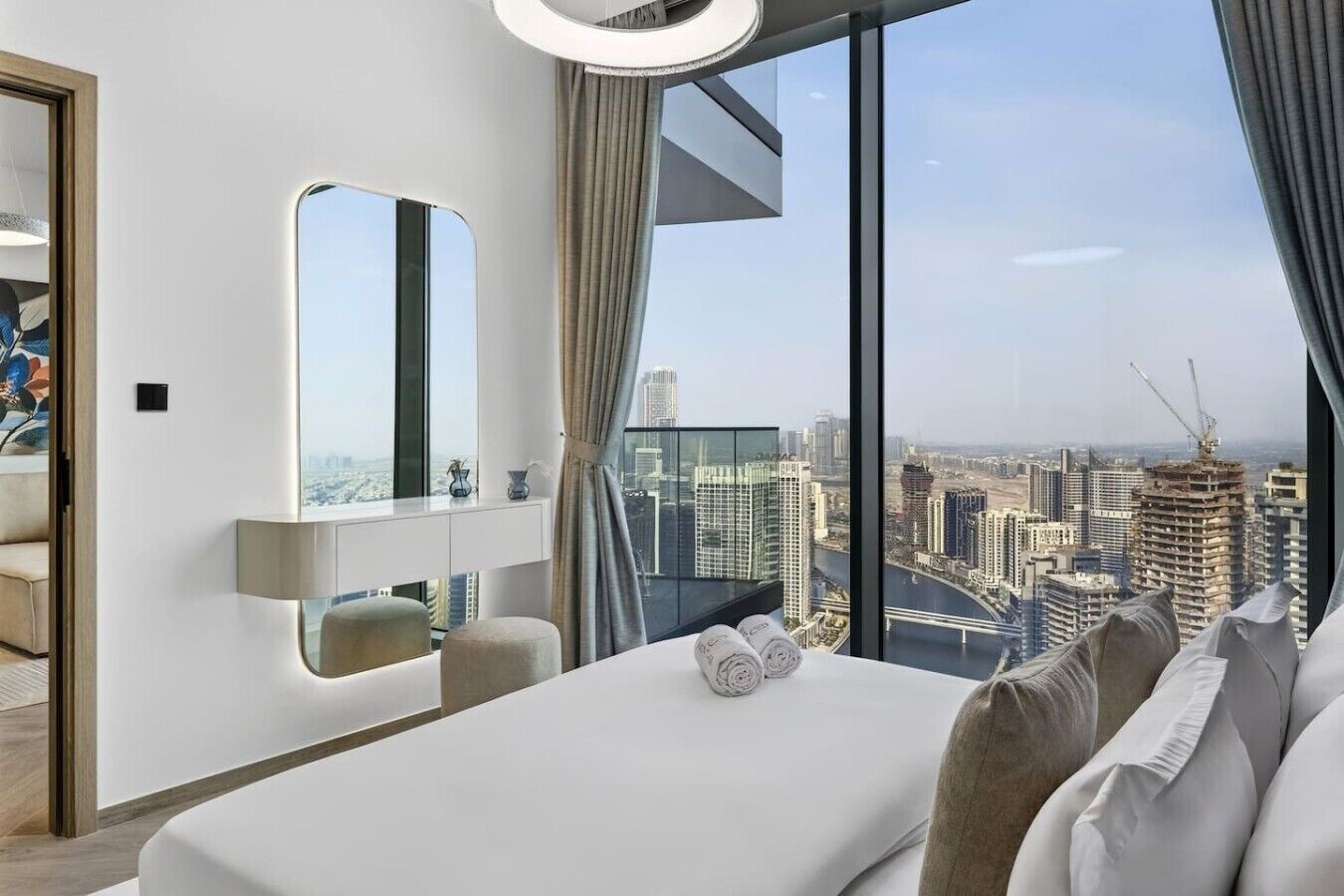 Een moderne hotelkamer met een groot bed, nachtkastje, spiegel en uitzicht op een stadsbeeld.