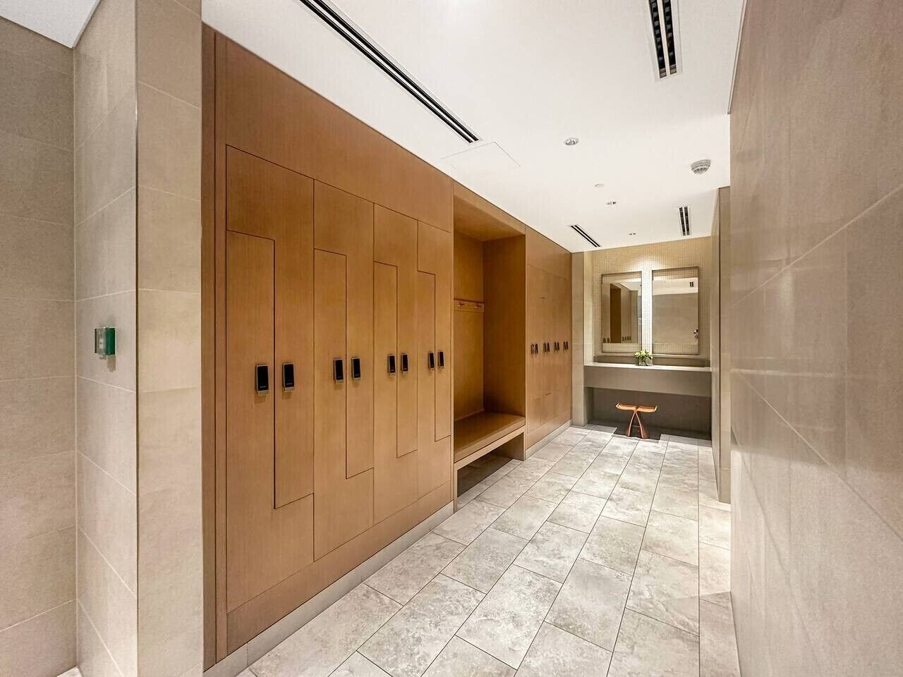 A modern bathroom with wooden lockers, a bench, and a large mirror.