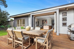 Eine Terrasse im Freien mit Holztisch und -stühlen, einem Grill und Blick ins Haus.