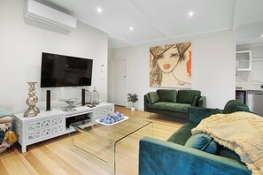 A modern living room with a flat-screen TV, a green sofa, a white console table, and a painting on the wall. - Bella Rye by Ready Set Stay (Rye)