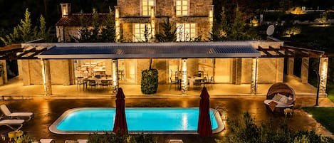 A two-story stone house with a swimming pool, outdoor dining area, and lounge chairs.