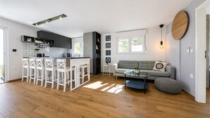 Een moderne keuken met een centraal eiland, witte barkrukken, een grijze bank en een ronde houten accentmuur.