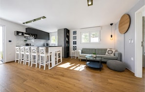 A modern kitchen with a central island, white bar stools, a grey sofa, and a round wooden accent wall. - Amazing home in Zerava (Zerava)