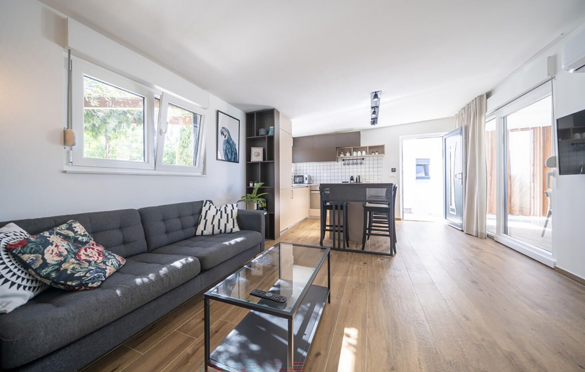 Una sala moderna con un sofá, una mesa de centro de cristal y una zona de cocina con una mesa de comedor y sillas.