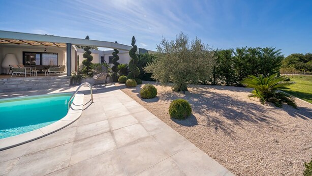 A pool area with a clear sky, a covered seating area, and well-maintained landscaping. - Stunning home in Zerava (Zerava)