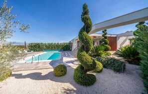 A modern outdoor pool area with a clear sky, surrounded by neatly trimmed hedges and a gravel path. - Stunning home in Zerava (Zerava)