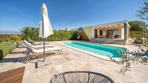Et moderne poolområde med liggestole og et overdækket opholdsområde.