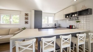 Et moderne køkken med en stor ø, barstole, en indbygget ovn og et spiseområde med en sofa.