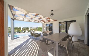 Un patio moderno al aire libre con piscina, una mesa de madera, sillas de mimbre y una lámpara blanca grande.