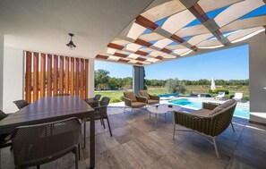 Eine überdachte Terrasse mit Pool, Gartenmöbeln und Landschaftsblick.