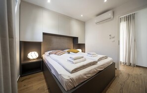 Un dormitorio moderno con una cama grande, cabecero incorporado, mesitas de noche y un equipo de aire acondicionado.