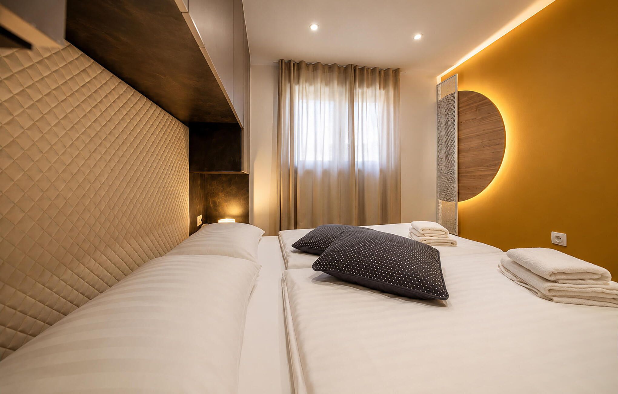 A hotel room with a bed, pillows, a mirror, and a window with curtains.