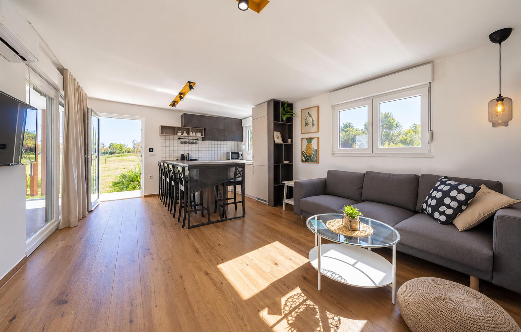 Et moderne opholdsrum med et køkken, spiseplads og en sofa med et sofabord i glas.
