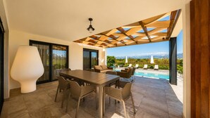 Ein moderner Essbereich im Freien mit Pool, einer Holzpergola und Blick auf Berge.