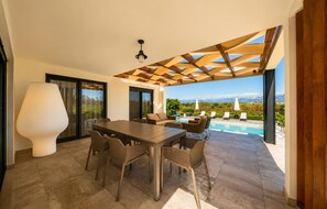 Ein moderner Essbereich im Freien mit Pool, einer Holzpergola und Blick auf Berge.