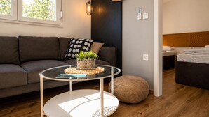 Ein modernes Wohnzimmer mit einer Couch, einem runden Glastisch, einem runden Hocker, einer Wandleuchte und einem Bett mit einem Holzkopfstück.