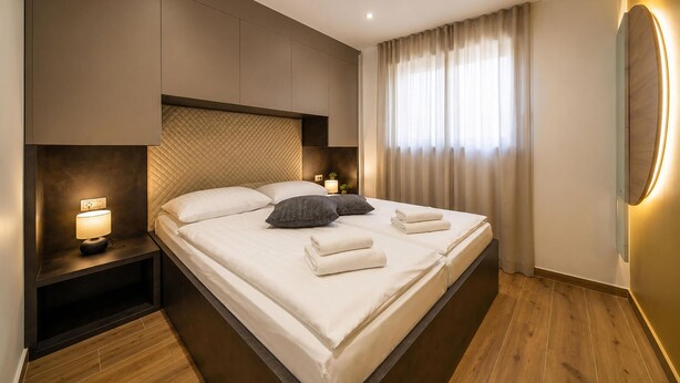 Ein modernes Hotelzimmer mit einem großen Bett, Nachttischlampen, einem Beistelltisch und Blick ins Freie durch ein Fenster mit Vorhängen.