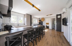 Eine moderne Küche mit einer langen Kochinsel, Barhocker, einem Einbauofen und einem großen Fenster.