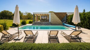Ein moderner Poolbereich im Freien mit Liegestühlen und Sonnenschirmen, umgeben von gepflegter Bepflanzung.