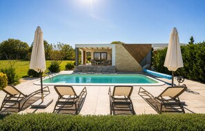 Ein moderner Poolbereich im Freien mit Liegestühlen und Sonnenschirmen, umgeben von gepflegter Bepflanzung.