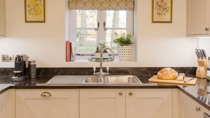 A kitchen with a sink, a window with a view, and a countertop with a coffee maker and books. - The Garden Collection at Woodhall Park | Sleeps 12 | Wood Fired Hot Tub (Watton at Stone)