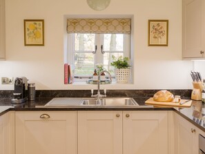 A kitchen with a sink, a window with a view, and a countertop with a coffee maker and books. - The Garden Collection at Woodhall Park | Sleeps 12 | Wood Fired Hot Tub (Watton at Stone)