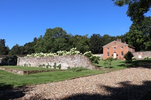 A historic brick building with a garden, a stone wall, and a gravel path. - The Garden Collection at Woodhall Park | Sleeps 12 | Wood Fired Hot Tub (Watton at Stone)