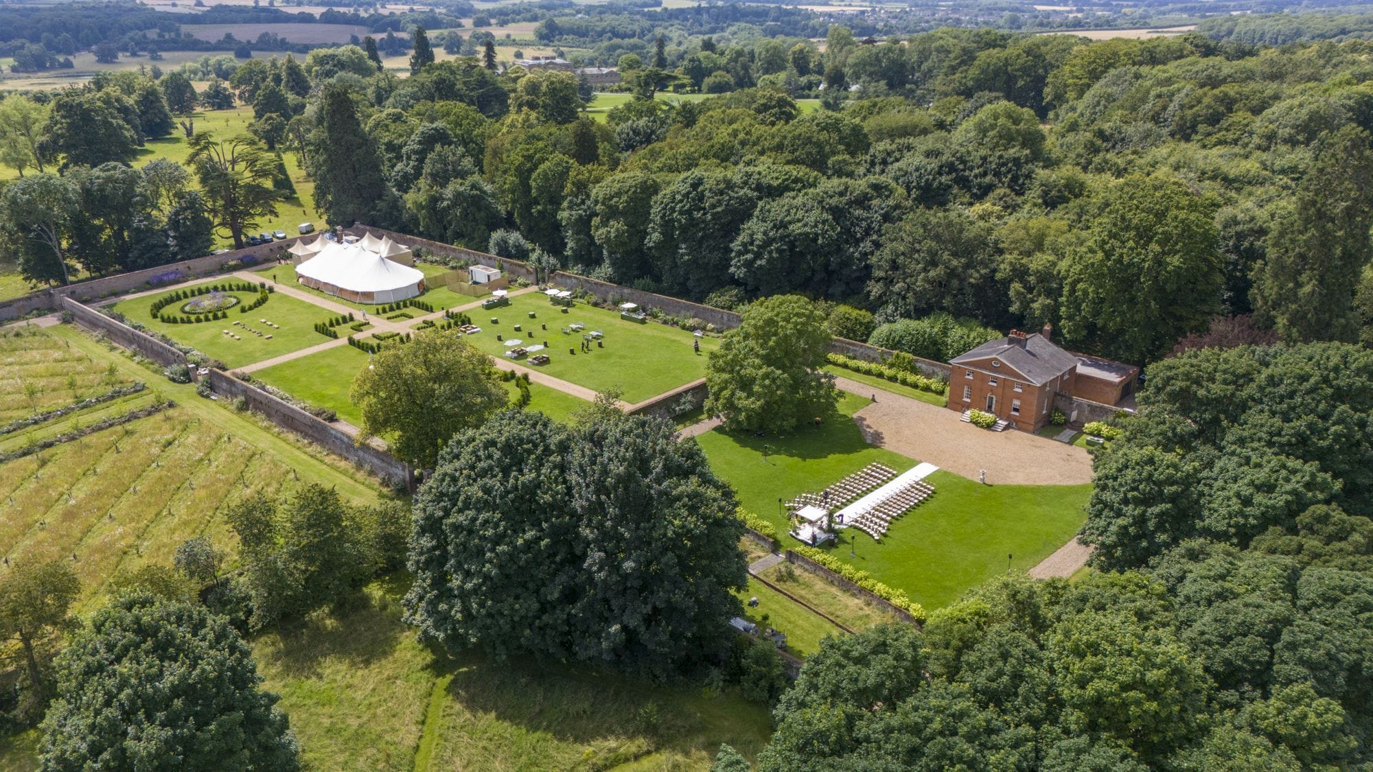 An aerial view of a large estate with a central lawn, a circular garden, and a brick building.