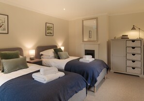 A hotel room with two beds, a fireplace, a dresser with drawers, and framed artwork on the walls. - The Garden Collection at Woodhall Park | Sleeps 12 | Wood Fired Hot Tub (Watton at Stone)