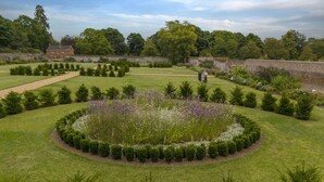 A well-maintained garden with a circular flower bed, neatly trimmed hedges, and a brick wall in the background. - The Garden Collection at Woodhall Park | Sleeps 12 | Wood Fired Hot Tub (Watton at Stone)