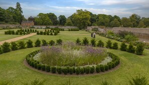 A well-maintained garden with a circular flower bed, neatly trimmed hedges, and a brick wall in the background. - The Garden Collection at Woodhall Park | Sleeps 12 | Wood Fired Hot Tub (Watton at Stone)