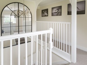 A staircase with white railings, a chandelier, and wall-mounted artwork. - The Garden Collection at Woodhall Park | Sleeps 12 | Wood Fired Hot Tub (Watton at Stone)