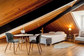 Ein gemütliches Schlafzimmer im Dachgeschoss mit einem Bett, zwei Sesseln, einem kleinen Tisch und einer Lampe.