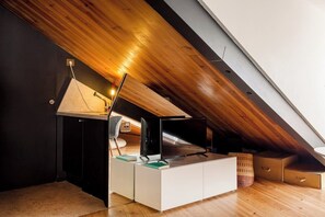 Ein modernes Schlafzimmer im Loft-Stil mit geneigter Decke, integriertem Schreibtisch mit Computer und einer gemütlichen Sitzecke.