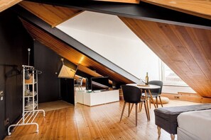 Ein Loft-Zimmer mit schrägem Dach, einer weißen Unterhaltungseinheit, einem Esstisch mit Stühlen und einer Couch.