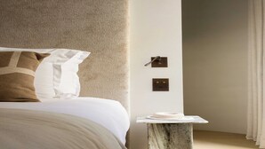 Quarto moderno com cama, mesa de cabeceira de mármore e interruptor de luz na parede.