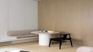 Quarto moderno com mesa redonda branca, uma cadeira preta, um sofá bege e parede de madeira clara.