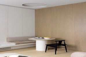 A modern room with a round white table, a black chair, a beige sofa, and a light wooden wall. - Luxurious suite - AC- 2P- Madeleine/Saint Honore (Paris)
