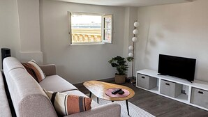 Ett modernt vardagsrum med en soffa, ett soffbord, ett TV-bord och ett fönster med utsikt.