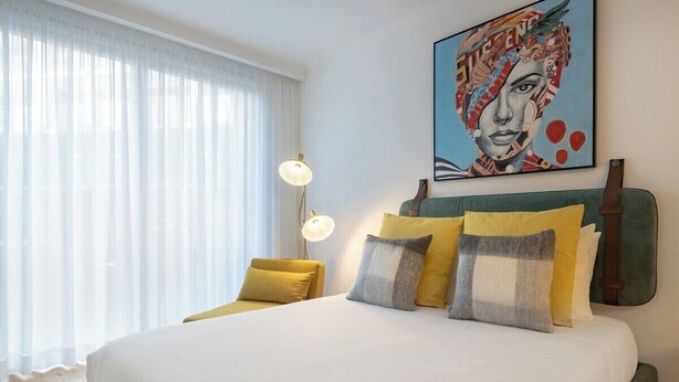 A hotel room with a large bed, a painting on the wall, and a window with sheer curtains. - Formosa City Studio (Porto)